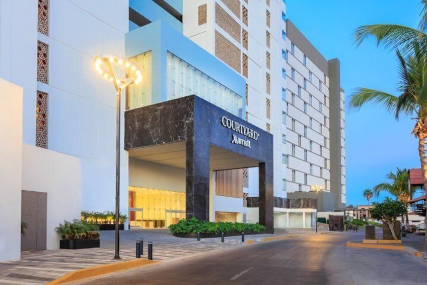A Courtyard Marriott hotel entrance with a modern design, palm trees, and a well-lit street. 2