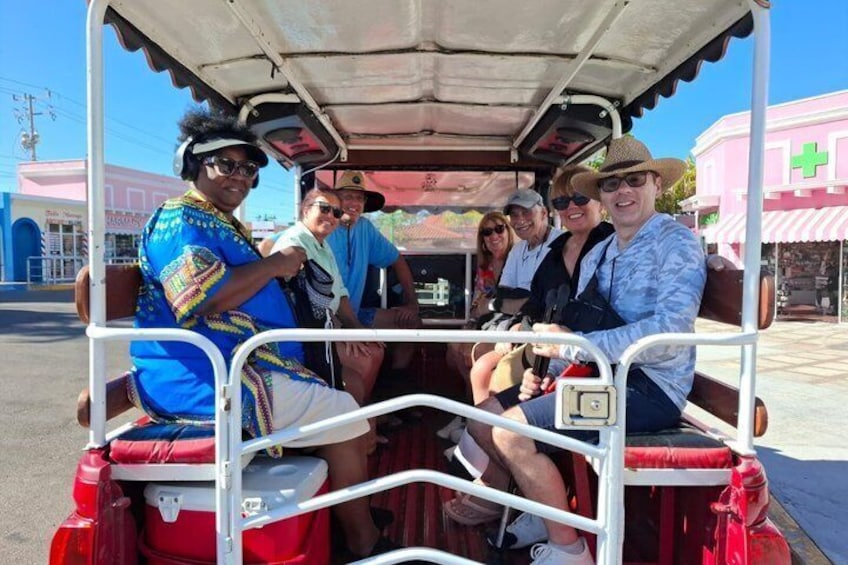 A group of people on a stationary vehicle with a canopy, parked in an urban area with buildings in the background. 1