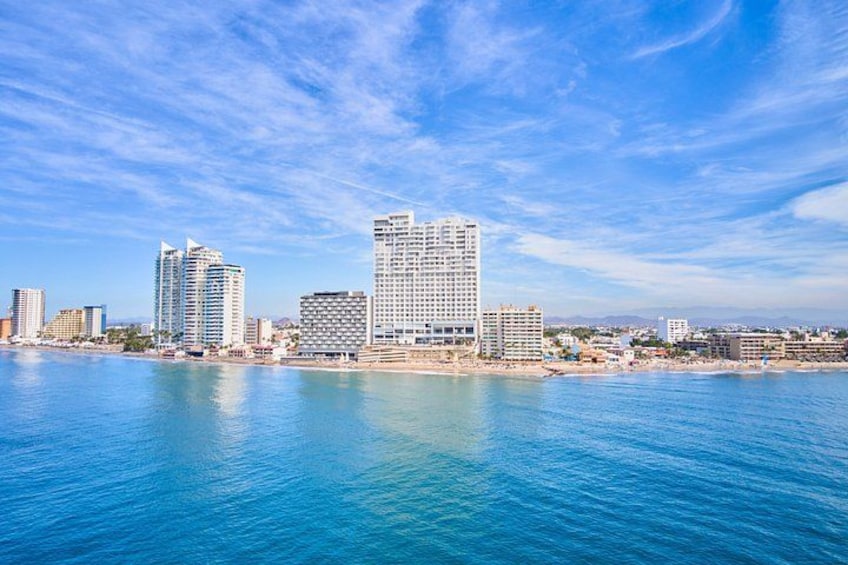 A coastal cityscape with high-rise buildings, a clear blue sky, and calm sea. 5