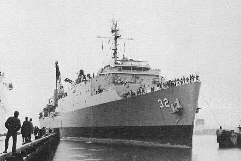 A large ship with the number 32-14 on its side, docked at a pier with people standing on the deck. 4