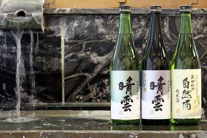 Three bottles with Japanese text on a marble surface with a water feature in the background. 1