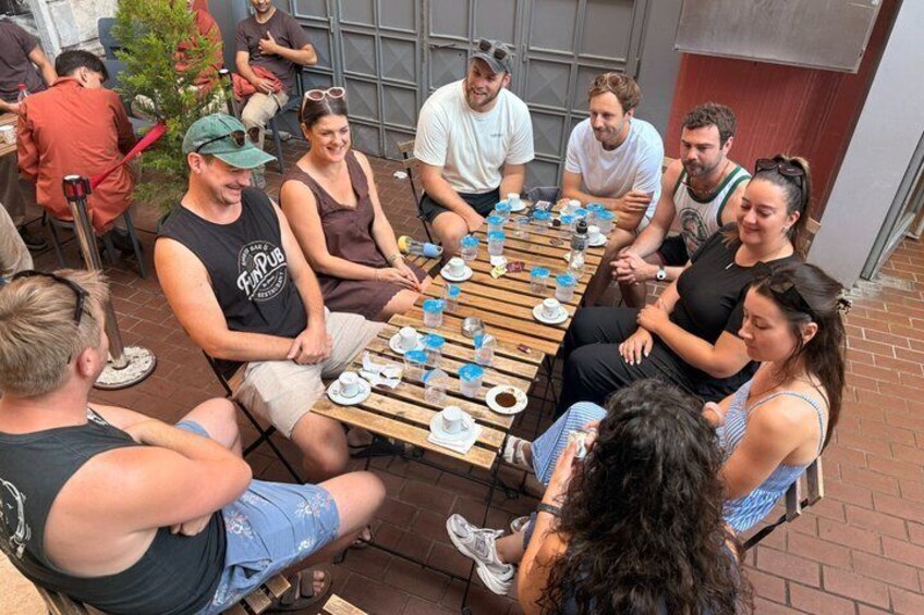 A group of people seated around a wooden table outdoors, engaged in conversation. 5