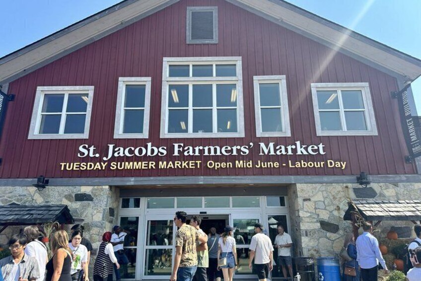 A red building with a sign that reads 'St. Jacobs Farmers' Market' and mentions a Tuesday Summer Market. 1
