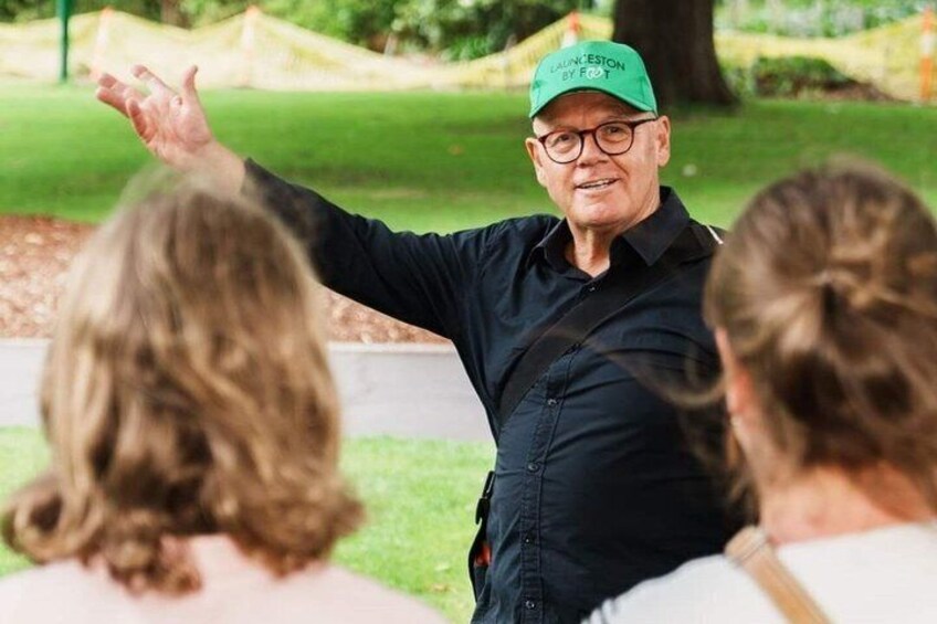 A person in a green cap and dark shirt gesturing to two people. 1