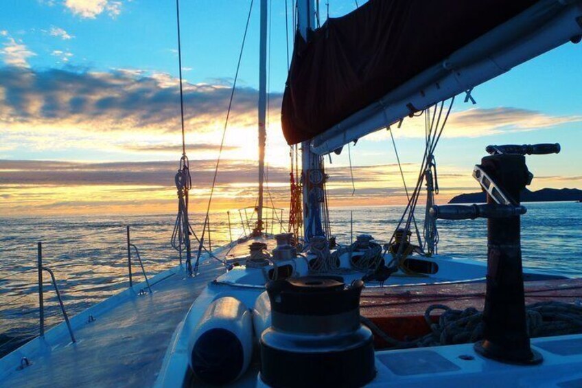 A sailboat at sunset with the ocean and a distant landmass. 2