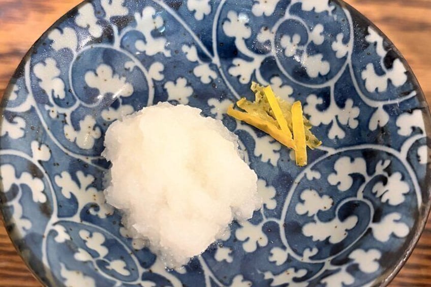 A blue and white patterned plate with a mound of white rice and a piece of yellow ginger. 5