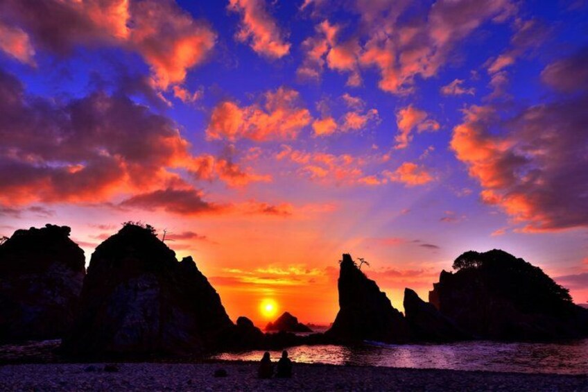 A sunset over a rocky coastline with silhouettes of cliffs and a calm sea. 2