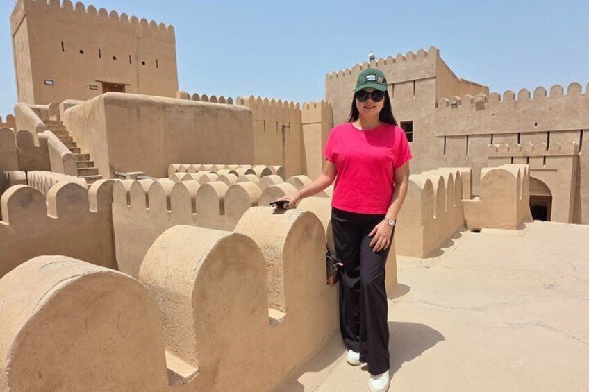 A person standing in front of a large, beige, fortress-like structure with crenellated walls and a staircase leading to a tower. 2