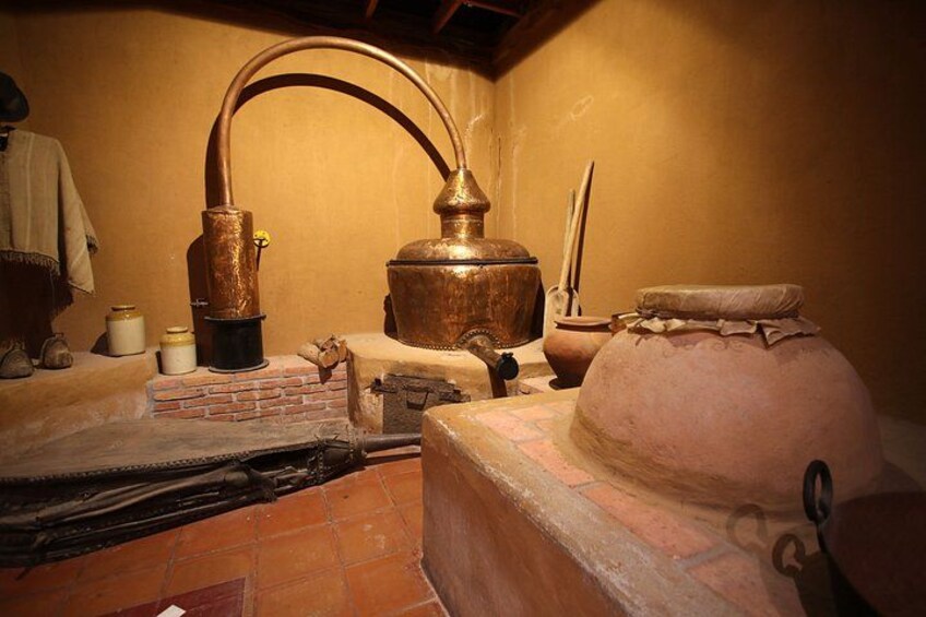 A traditional kitchen with a large copper still, a brick oven, and various cooking utensils. 3