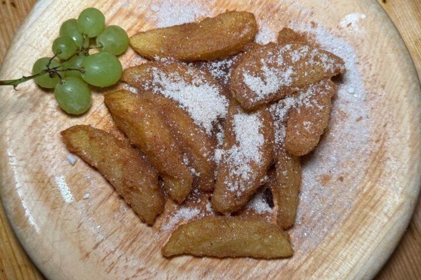 A wooden plate with fried dough sticks dusted with powdered sugar and a bunch of green grapes. 2