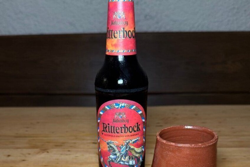 A bottle of Kaltenbrunner Ritterbock beer with a label, next to a clay mug on a wooden surface. 3