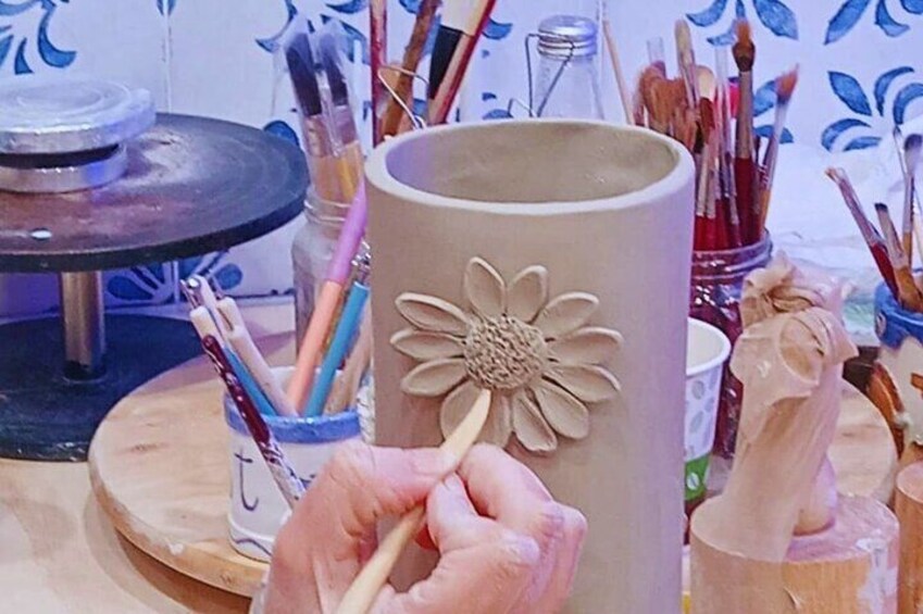 A person painting a flower on a ceramic mug. 1