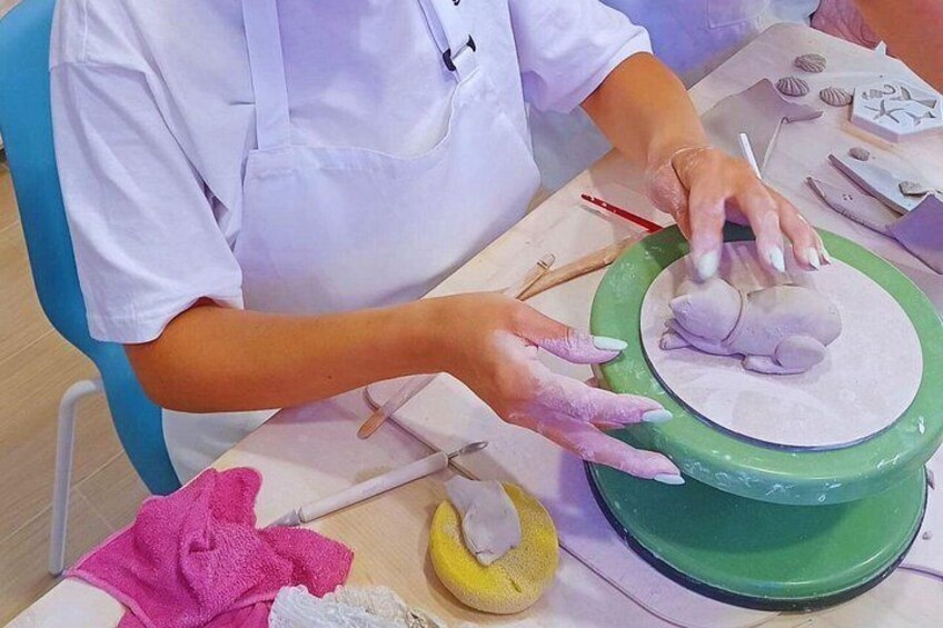 A person wearing a white apron, working with clay on a green pottery wheel. 3