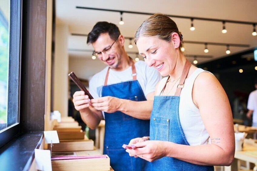 Two people in aprons, one holding a smartphone, in a cafe with wooden tables and chairs. 1