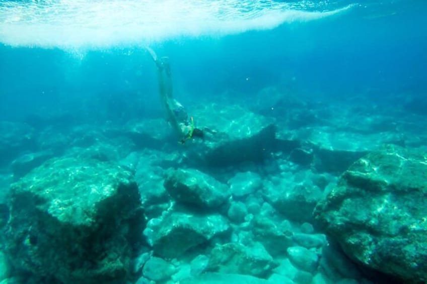 A diver underwater with rocks and clear water. 3