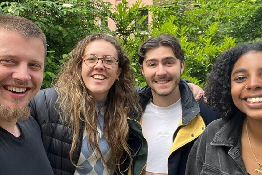 Four people standing outdoors with greenery in the background. 2