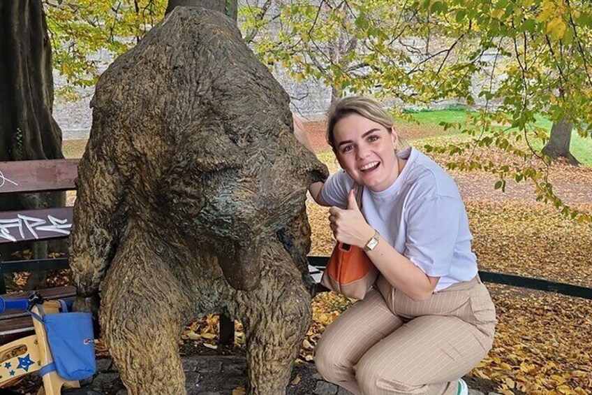 A person crouching next to a large bear statue in a park. 5