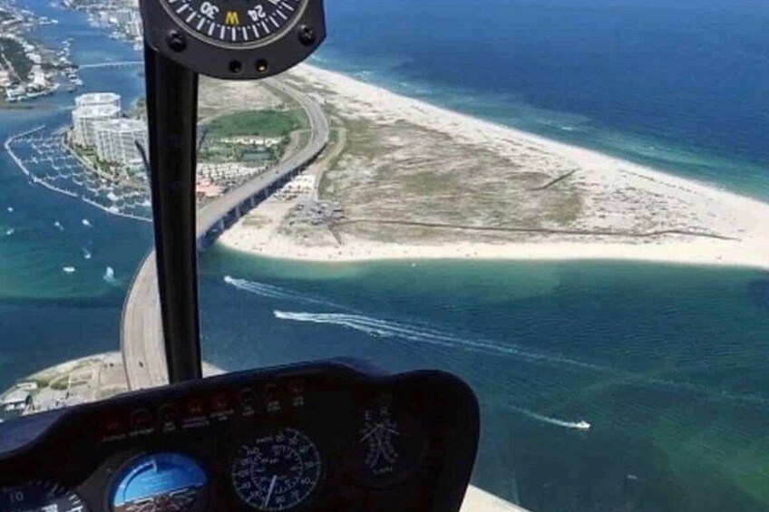 A helicopter cockpit with a view of a coastal area, including a beach and a marina. 3