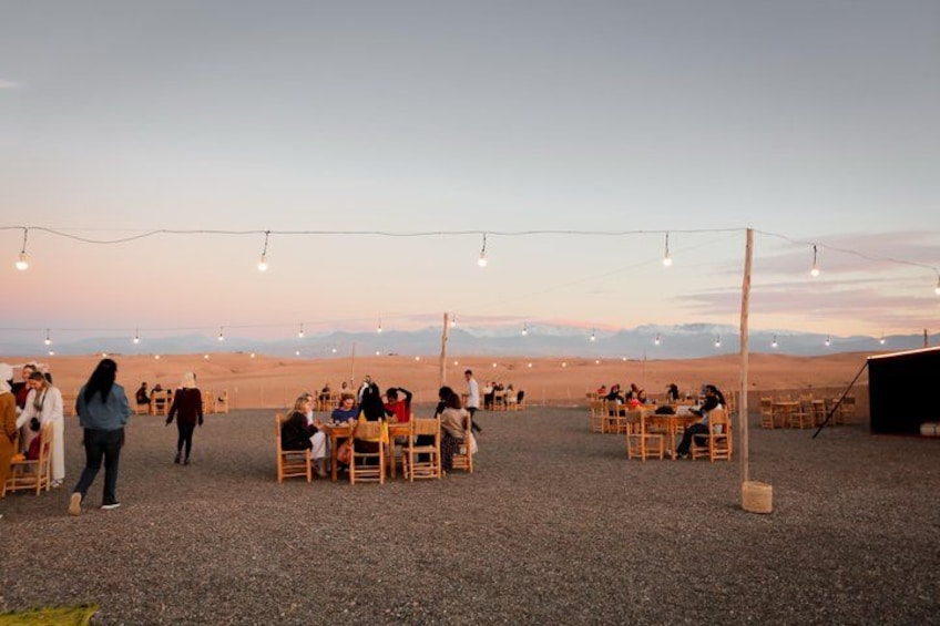 An outdoor dining area with tables and chairs set up on a gravel surface, with a mountainous backdrop. 2