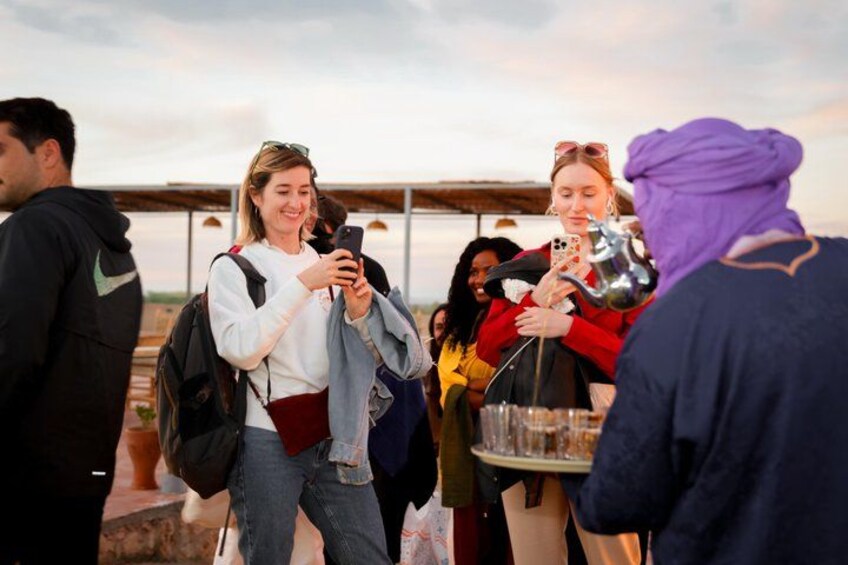 A group of people outdoors, some using smartphones, and one person pouring a drink from a metal container. 4