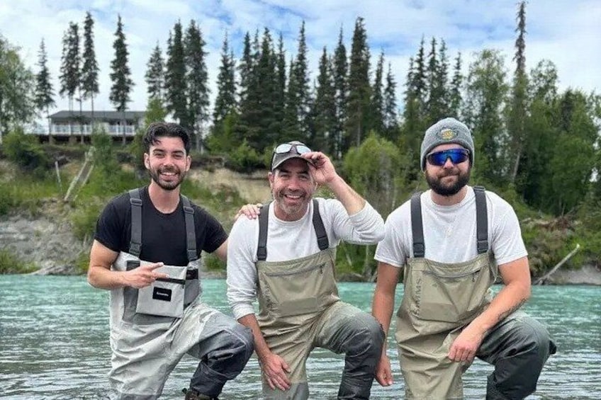 Three people standing by a river with trees in the background. 2