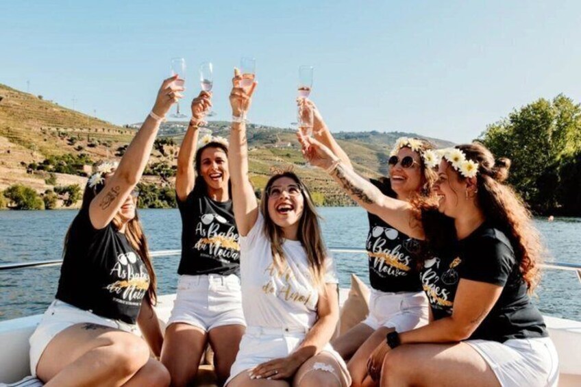 A group of people on a boat, holding up glasses, with a body of water and hills in the background. 3