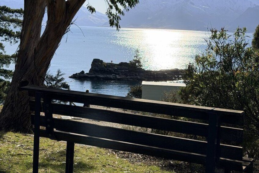 A bench overlooking a calm lake with a rocky outcrop in the distance and mountains in the background. 2