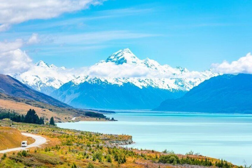 A lake with mountains in the background, a road, and a vehicle. 4