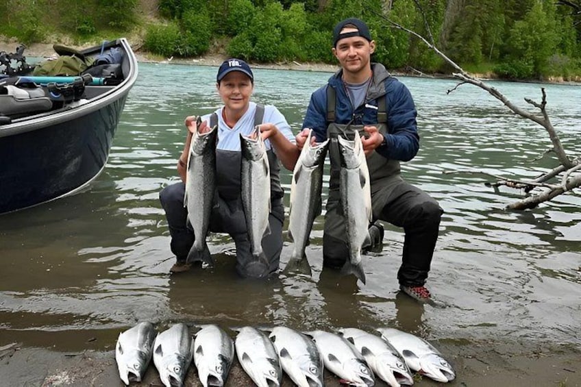 Two people holding fish in a river with a boat in the background. 4