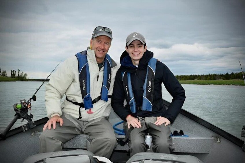 Two people on a boat with fishing rods, wearing life jackets, and a cloudy sky in the background. 2