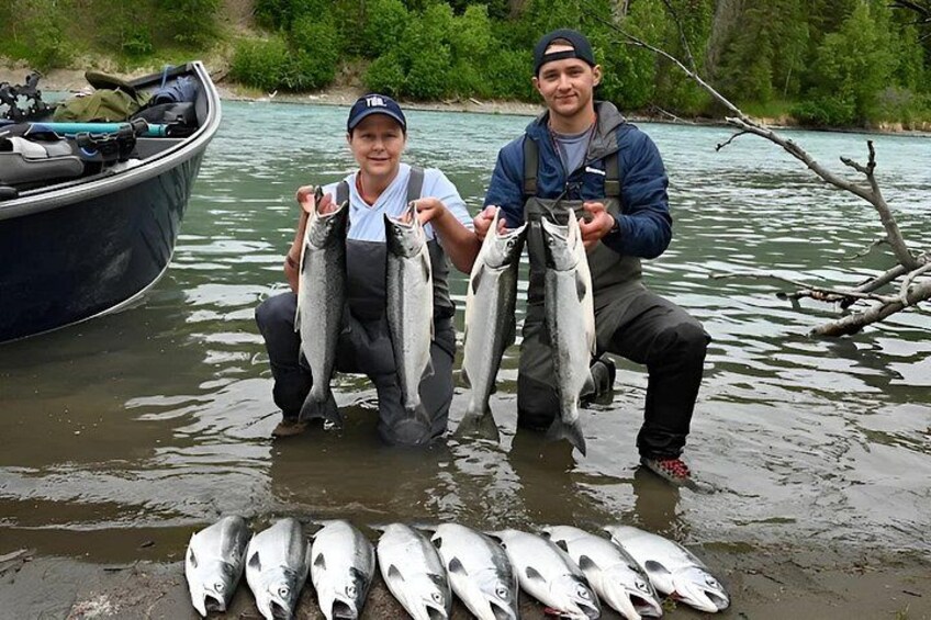 Two people holding fish in a river with a boat in the background. 4