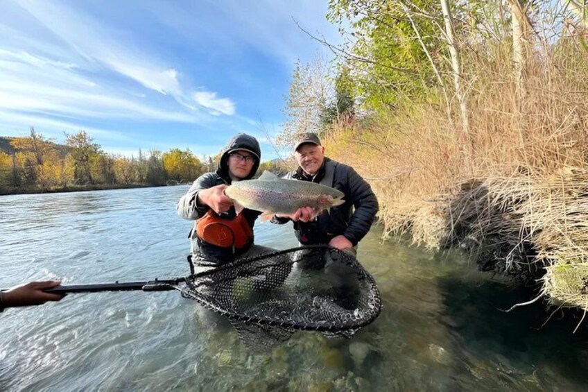 Two people standing in a river, one holding a fish. 3