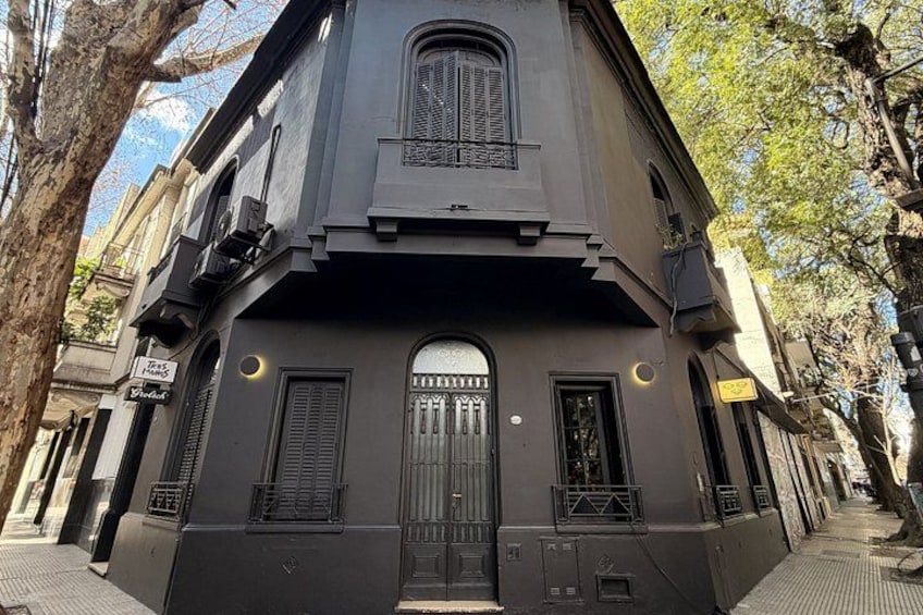 A dark-colored building with a large arched window and a door, flanked by two smaller windows with shutters. 3