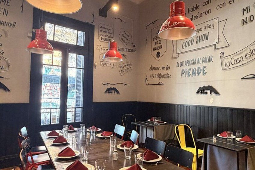 A restaurant interior with tables set for dining, red pendant lights, and walls decorated with various phrases in Spanish. 4