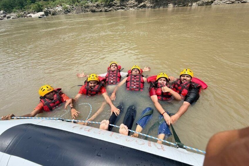 A group of people in a boat wearing life jackets and helmets, floating on a river. 3
