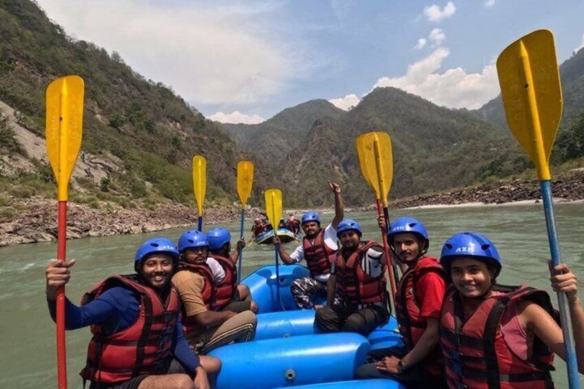 A group of people in a blue raft on a river, wearing helmets and life vests, paddling with yellow paddles. 2