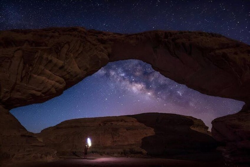 A starry night sky framed by a natural rock arch with a single light source at the base. 2