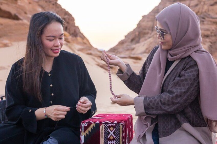 Two people sitting on a desert with a camel and a red bag with a star pattern. 3