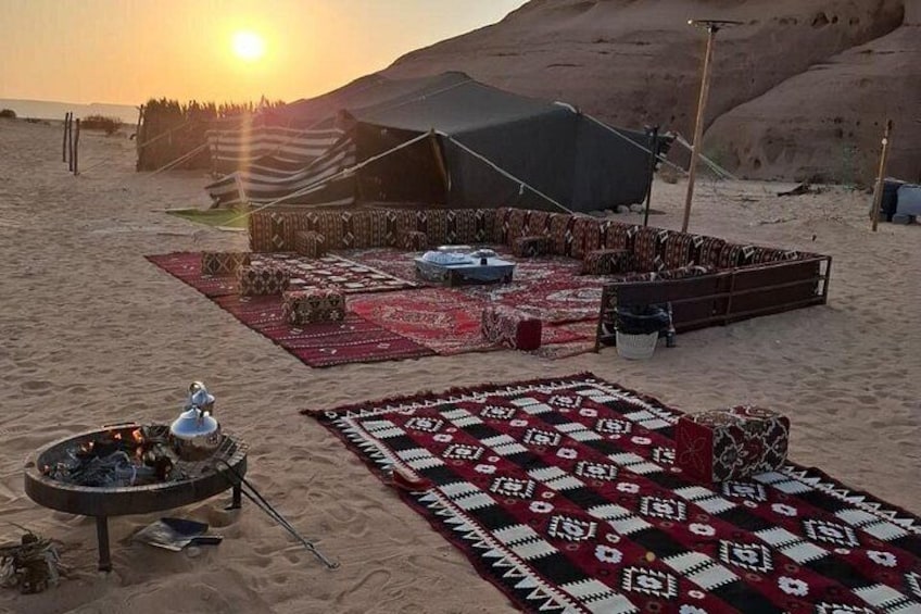 A desert campsite with tents, blankets, and a fire pit at sunset. 5