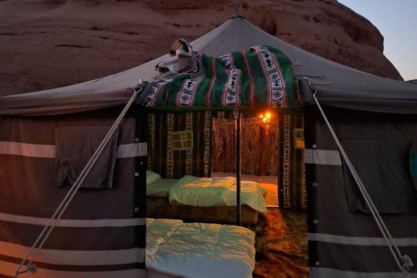 A tent with a patterned canopy, a bed, and a small table with a light source. 2