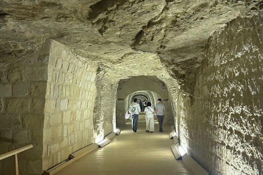 A stone tunnel with a wooden walkway and people walking inside. 4
