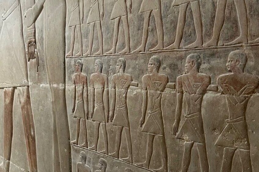 A stone relief with figures in ancient Egyptian attire, hieroglyphs, and a partial depiction of a deity. 3
