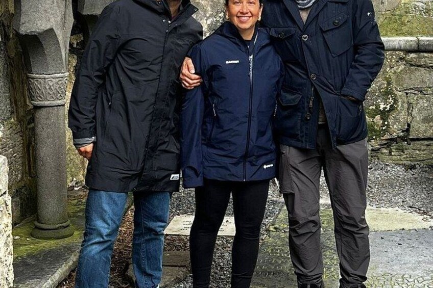 Three people standing in front of a stone structure with moss. 3
