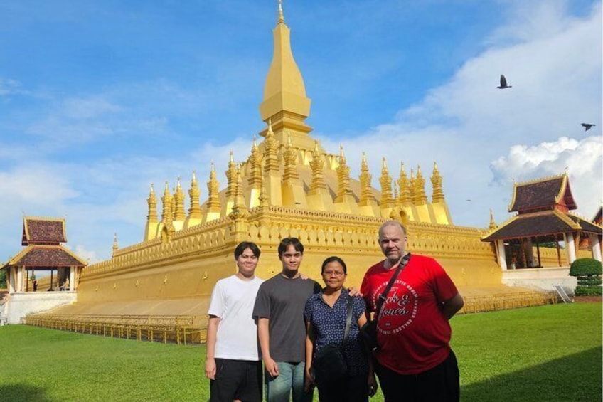 A golden temple with multiple spires and a large central spire, surrounded by a grassy area and smaller buildings. 1
