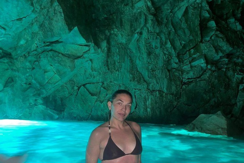 A person in a black bikini standing in a turquoise pool with rocky cave walls in the background. 4