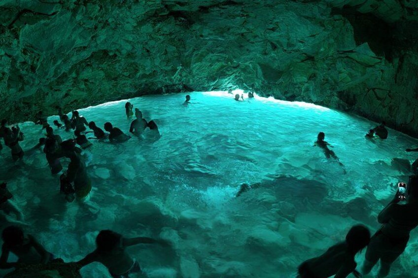 A group of people swimming in a natural pool surrounded by rocky cave walls. 1