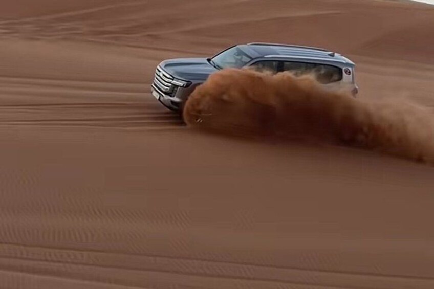 A vehicle driving through a desert with sand dunes. 4