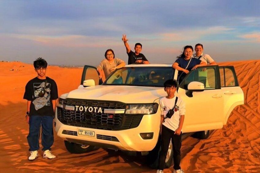 A white Toyota SUV parked in a desert with people standing around it. 1