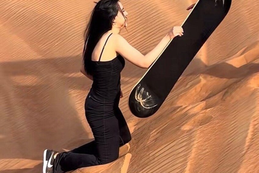 A person in a black dress holding a snowboard, standing on a sandy slope. 5