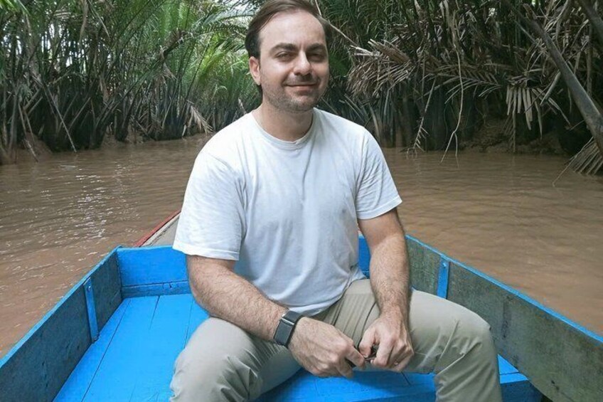 A man in a blue boat on a river surrounded by mangrove trees. 3